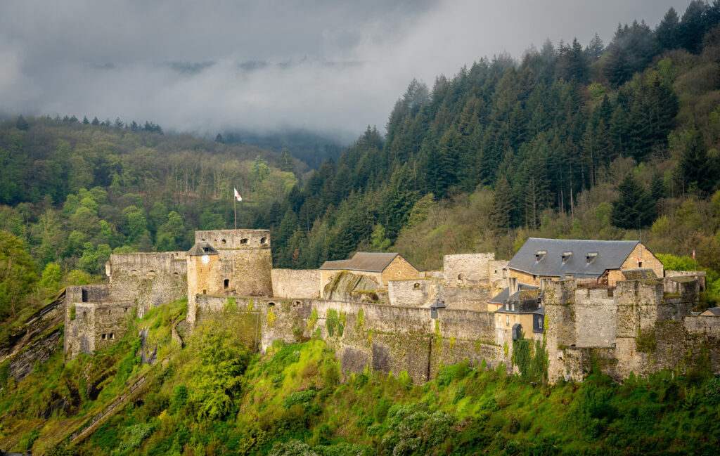 Château de Bouillon von der Semois aus: Blick auf das imposante mittelalterliche Château de Bouillon vom Fluss aus, umgeben von grünen Tälern und schroffen Felsen.