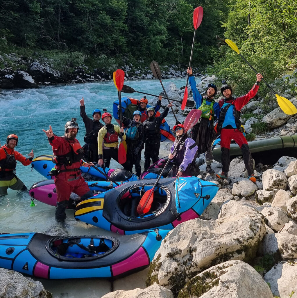 Groep packrafters lacht en praat samen aan de oever van de Soča rivier tijdens de European Packrafting Meet-up