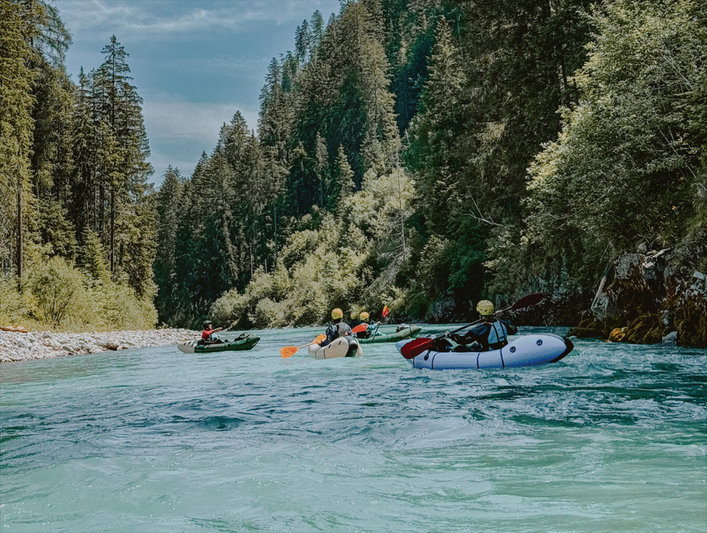 Avonturiers varen in packrafts door een helderblauwe rivier omringd door hoge dennenbomen