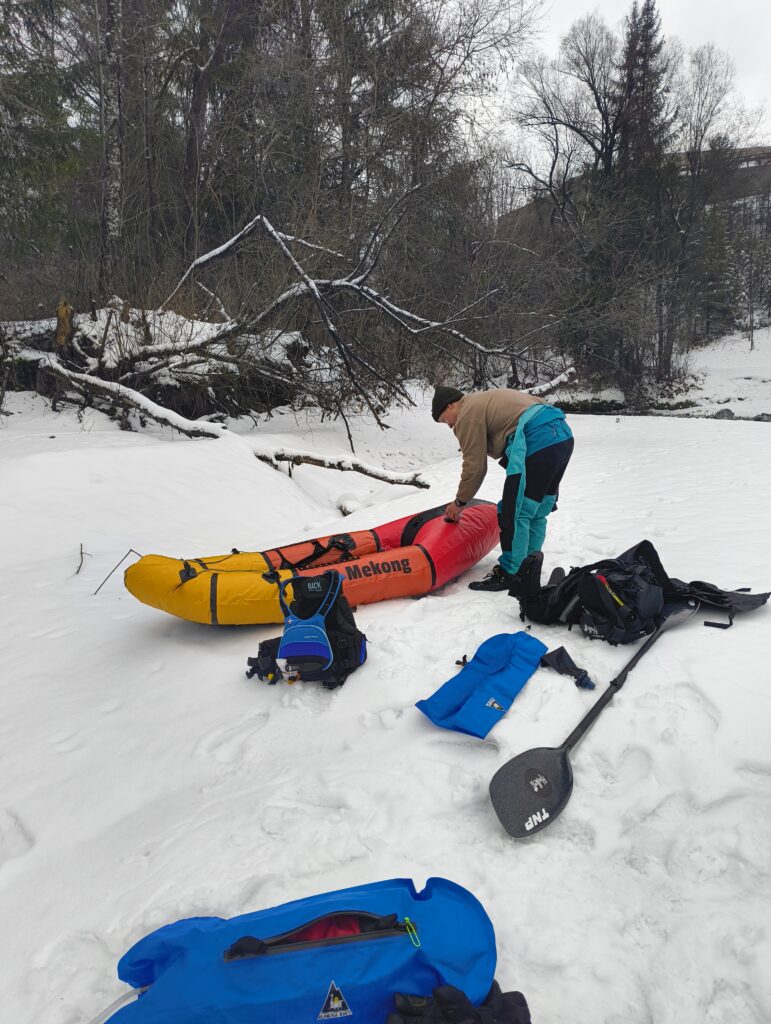 Packrafter paddles down quiet winter river with fog and bare trees
